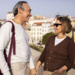 Happy Pensioners Couple Holding Hands Walking With Backpack Outdoors